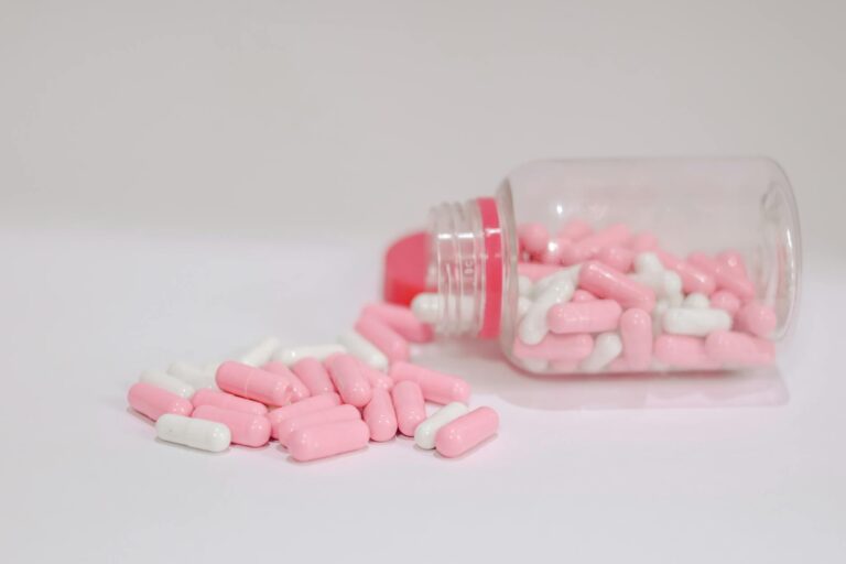 Close-up of pink and white capsules spilled from a plastic bottle on a white background.