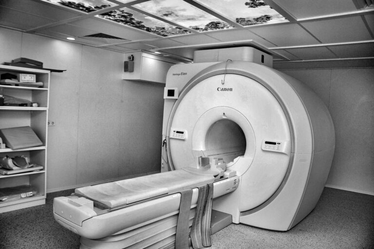 Black and white image of a modern MRI machine in a hospital room with overhead ceiling art.