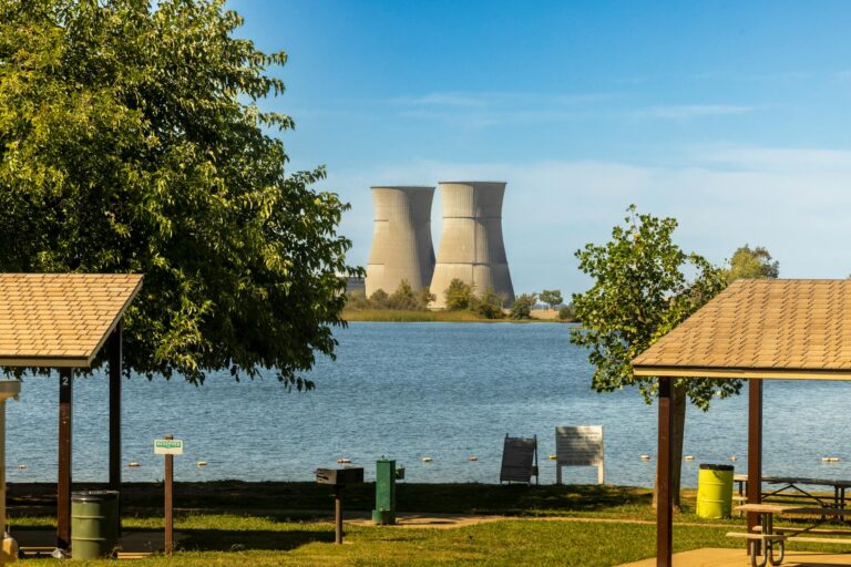 Cooling towers visible from a park by the lake during a sunny day with clear skies.