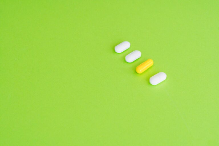 A row of white and yellow capsules on a green surface symbolizing medicine concept.
