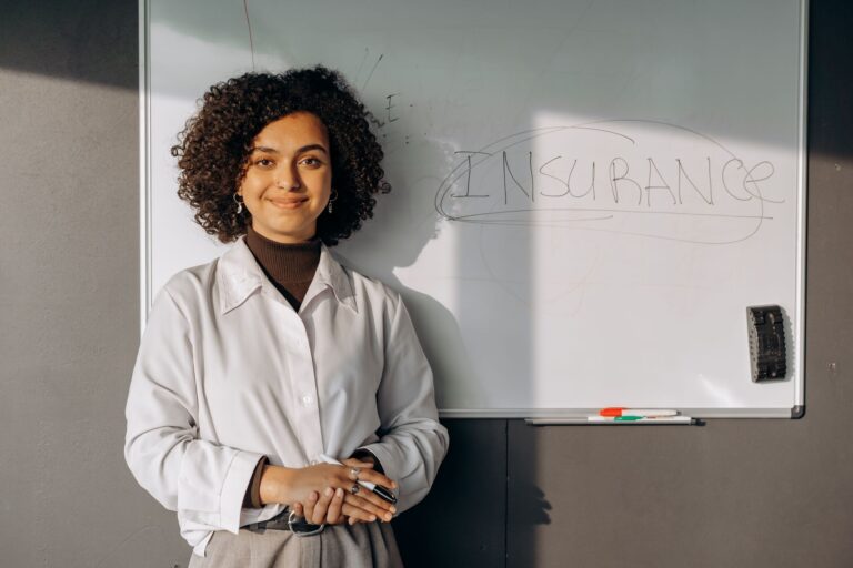 Smiling woman with curly hair standing by a whiteboard with 'insurance' written on it, conveying professionalism.