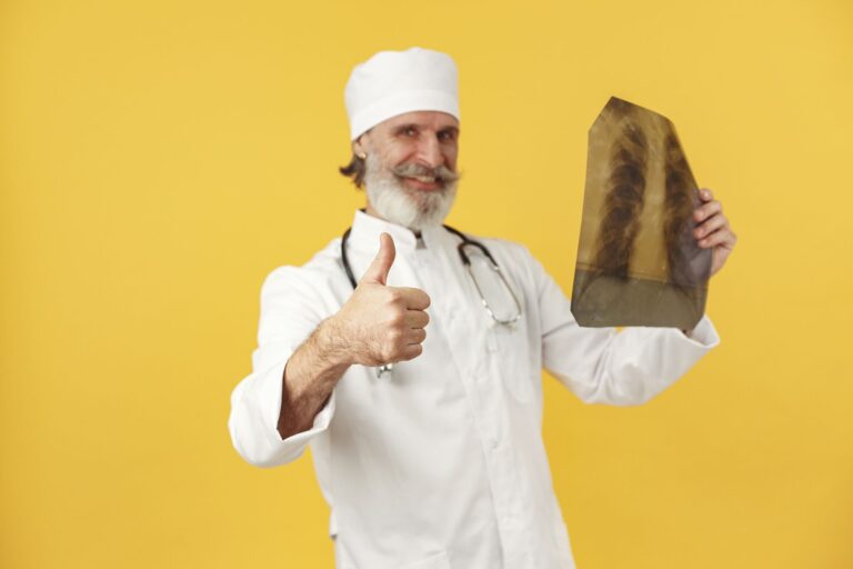 Smiling elderly doctor holding an X-ray and giving a thumbs-up in a cheerful studio setting.