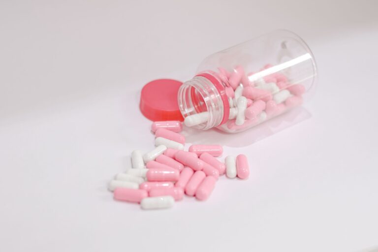 Pink and white capsules scattered from a tipped-over bottle on a white surface, symbolizing health care.